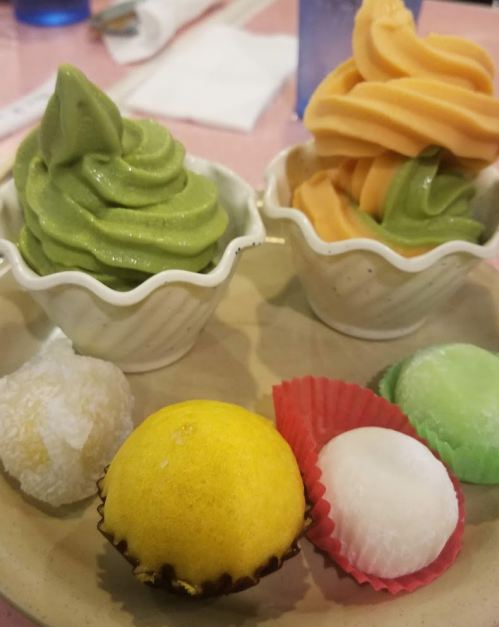 Two bowls of soft serve ice cream in green tea and orange flavors, with assorted mochi on a plate.