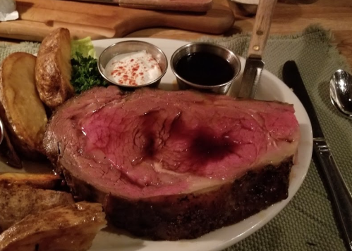 A plate of medium-rare prime rib with dipping sauces, roasted potatoes, and a garnish of lettuce.