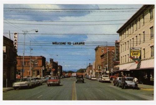 A vintage postcard of Laramie, featuring a street view with shops, cars, and a "Welcome to Laramie" sign overhead.