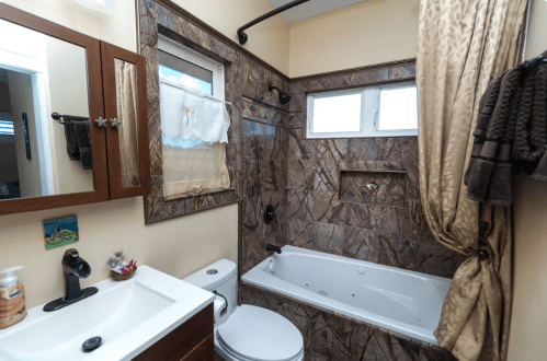 A small bathroom featuring a bathtub, sink, and decorative tile walls with natural light from two windows.