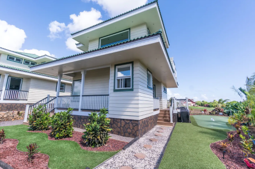 A modern two-story house with a porch, surrounded by landscaped greenery and a clear blue sky.