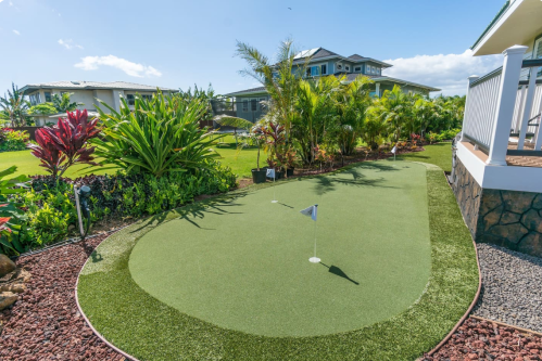 A well-maintained putting green surrounded by lush tropical plants and a modern house in the background.