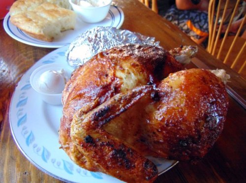 A plate featuring a whole roasted chicken, a baked potato wrapped in foil, and a side of butter.