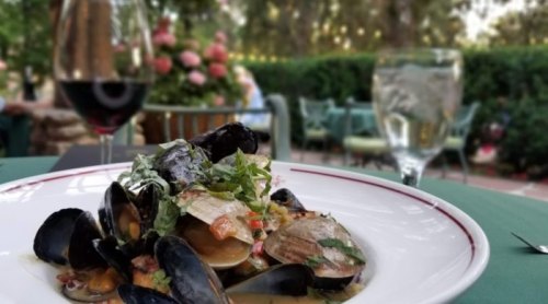 A plate of seafood pasta with clams and mussels, garnished with herbs, set on a green tablecloth with drinks in the background.