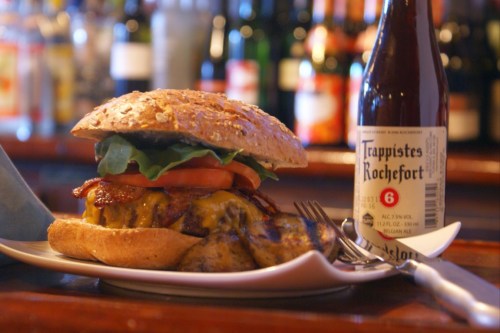 A hearty burger with cheese, bacon, lettuce, and tomato, served with a side of fries and a bottle of beer.