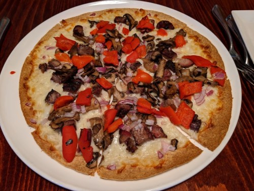 A round pizza topped with cheese, red peppers, mushrooms, onions, and chunks of meat on a thin crust.