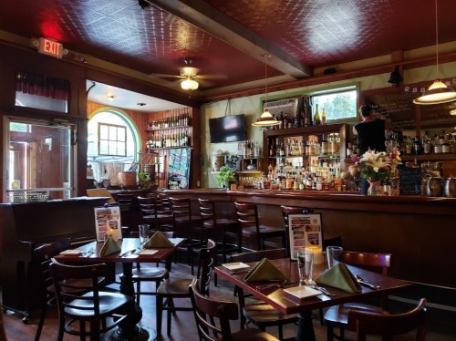 Cozy restaurant interior with a bar, wooden tables, and a bartender preparing drinks. Warm lighting and decor.