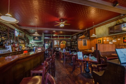 Cozy restaurant interior with wooden tables, a bar, and a red ceiling, creating a warm and inviting atmosphere.