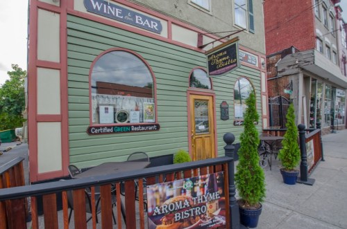 Exterior of Aroma Thyme Bistro, a green restaurant with a wine bar sign, featuring outdoor seating and potted plants.