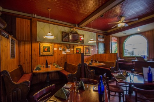 Cozy restaurant interior with wooden walls, red ceiling, and tables set with blue bottles and green napkins.