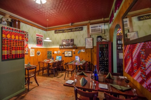 Cozy restaurant interior with wooden walls, tables set for dining, and colorful decor. Warm, inviting atmosphere.