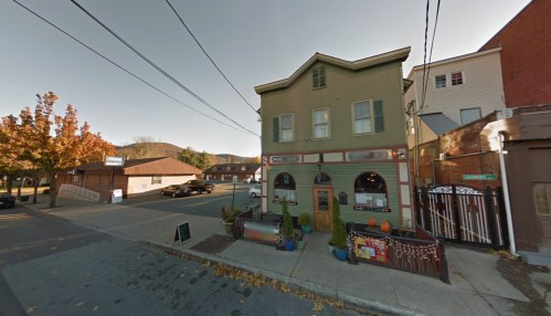 A quaint two-story building with a decorative facade, surrounded by trees and parked cars on a quiet street.