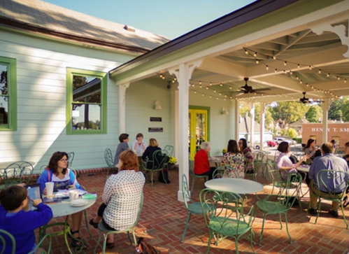 A cozy outdoor café with patrons enjoying drinks and conversation under string lights on a sunny day.