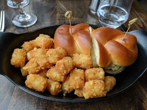 A cast iron skillet filled with crispy tater tots and two slider sandwiches with toothpicks.