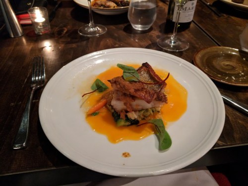 A plated dish featuring fish topped with crispy skin, served on a bed of vegetables and a vibrant orange sauce.