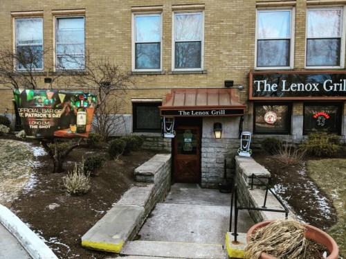 Entrance to The Lenox Grill, featuring a St. Patrick's Day banner and a stone staircase leading down.