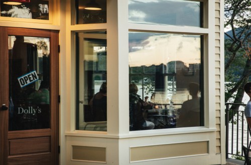 A cozy café named Dolly's with large windows reflecting a scenic view and patrons inside enjoying their time.