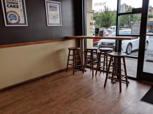 A cozy cafe interior with wooden stools by a large window, showcasing a view of parked cars outside.
