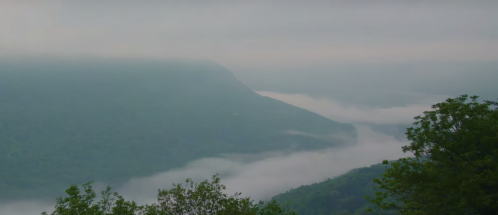 Foggy mountains with lush greenery and a river valley shrouded in mist, creating a serene, tranquil landscape.