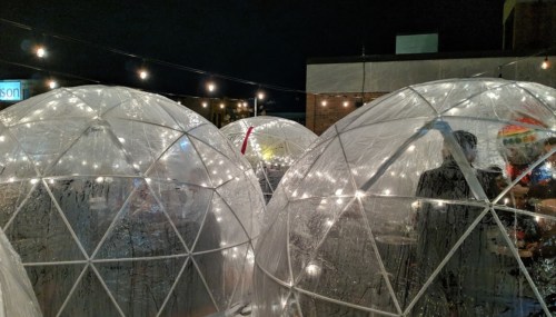 A cozy outdoor dining area with illuminated igloo-like structures under string lights at night.