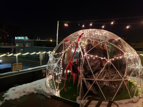 A cozy igloo-shaped structure with lights, people inside, and a snowy rooftop at night.