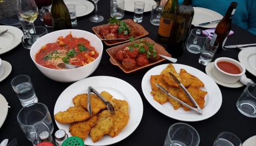 A table set with plates of pasta, meatballs, fried dishes, and drinks, surrounded by glasses and cutlery.
