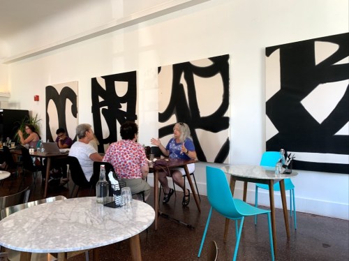 A group of people converses at a café with abstract black and white artwork on the walls and modern furniture.