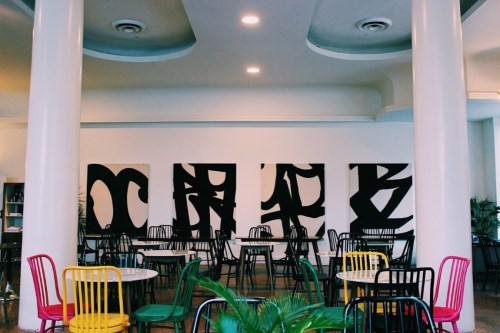 A modern café interior with colorful chairs, round tables, and abstract black artwork on the walls.