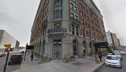 Historic brick building with ornate architecture, featuring a corner entrance and nearby parked cars.