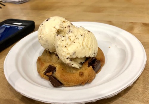 A chocolate chip cookie topped with two scoops of vanilla ice cream on a paper plate.