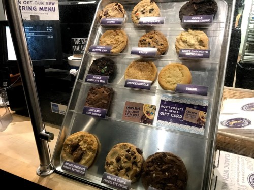 A display case filled with various cookie types, including chocolate chip, snickerdoodle, and white chocolate macadamia.