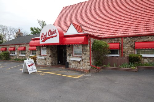 Exterior of a restaurant with a red roof and awnings, featuring a stone facade and a sign for gift certificates.