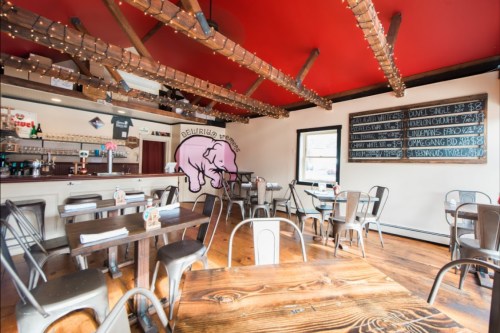 Cozy restaurant interior with wooden tables, metal chairs, a red ceiling, and a playful pig mural on the wall.