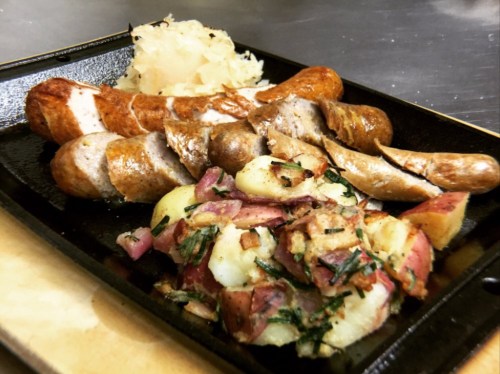 A plate of grilled sausages served with sauerkraut and a side of seasoned roasted potatoes.