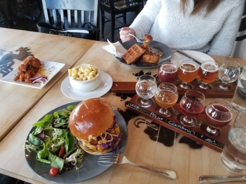 A table with a burger, salad, mac and cheese, chicken and waffles, and a flight of craft beers.