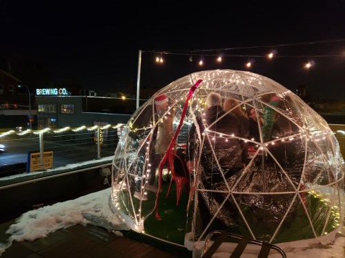 A festive igloo-shaped structure with lights, people inside, and a snowy rooftop at night.