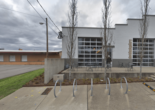 Exterior of a modern gallery building with large windows, bike racks in front, and overcast skies.