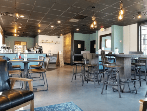 A modern café interior with wooden tables, metal chairs, and a coffee counter in the background. Soft lighting enhances the ambiance.