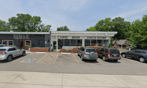A coffee shop and bakery with a sign reading "Scratch Kitchen," surrounded by parked cars and trees in the background.