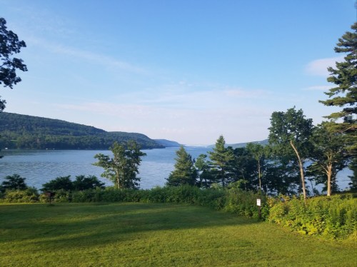 A serene lake view surrounded by lush greenery and rolling hills under a clear blue sky.