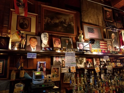 A bar with a wooden interior, featuring various portraits, flags, and memorabilia displayed on the walls and shelves.