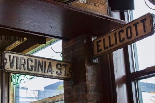 Two vintage street signs hanging indoors: one reads "VIRGINIA ST." and the other "ELLICOTT."