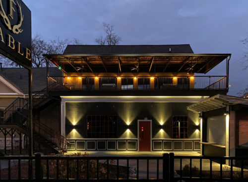 A modern building with a rooftop patio, illuminated at dusk, featuring a red door and stylish exterior lighting.