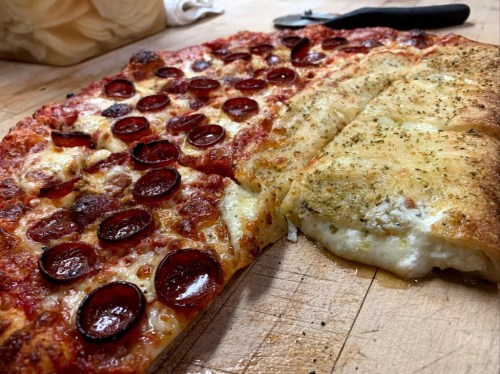 A close-up of a pizza with pepperoni and a side of cheesy breadsticks on a wooden surface.
