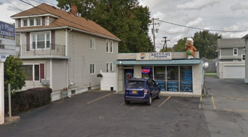 A pizzeria with a sign reading "Macy's Place," featuring a large inflatable figure outside and parked cars nearby.