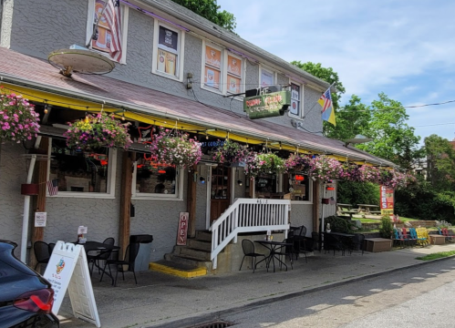 A charming restaurant with a colorful exterior, hanging flower baskets, and outdoor seating on a sunny day.