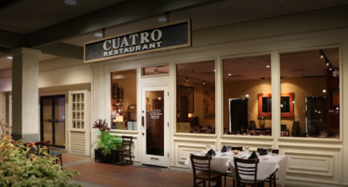 Exterior view of Cuatro Restaurant, featuring a welcoming entrance and outdoor seating in a shopping area.