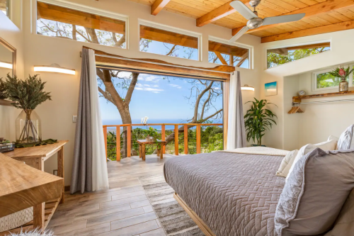 Cozy bedroom with large windows showcasing a scenic ocean view, wooden accents, and natural light.