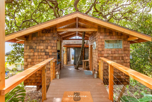 A charming wooden cabin with a welcoming mat, surrounded by lush greenery and trees.