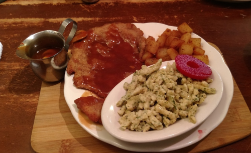 A plate of chicken fried steak with gravy, seasoned potatoes, and a side of pasta, garnished with a slice of beet.